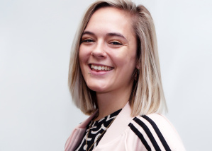 Image of Grace smiling at the camera, with blond shoulder length hair and a pink and black adidas tracksuit top over a black and white top.