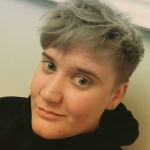 Image of Hannah with short grey/blond hair and a black hooded top