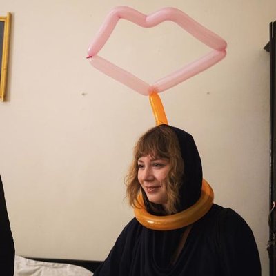Image of Eliza wearing a black hooded top. She has a funny balloon model of a pair of lips above her head.