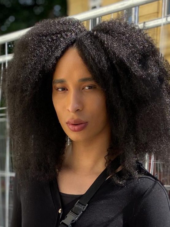 Image of Danielle Braithwaite-Shirley looking sideways at the camera. She has natural afro hair and is wearing a long black cardigan.