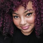 Headshot of Furaha, a young black woman smiling into camera with curly purple hair
