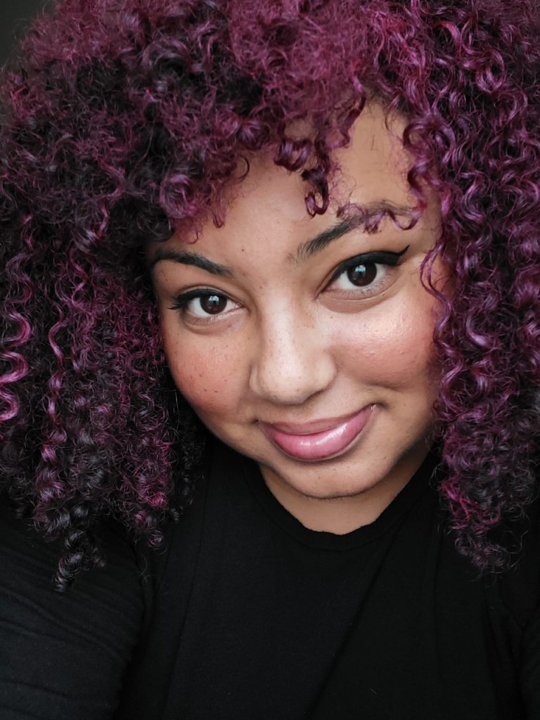 Headshot of Furaha, a young black woman smiling into camera with curly purple hair
