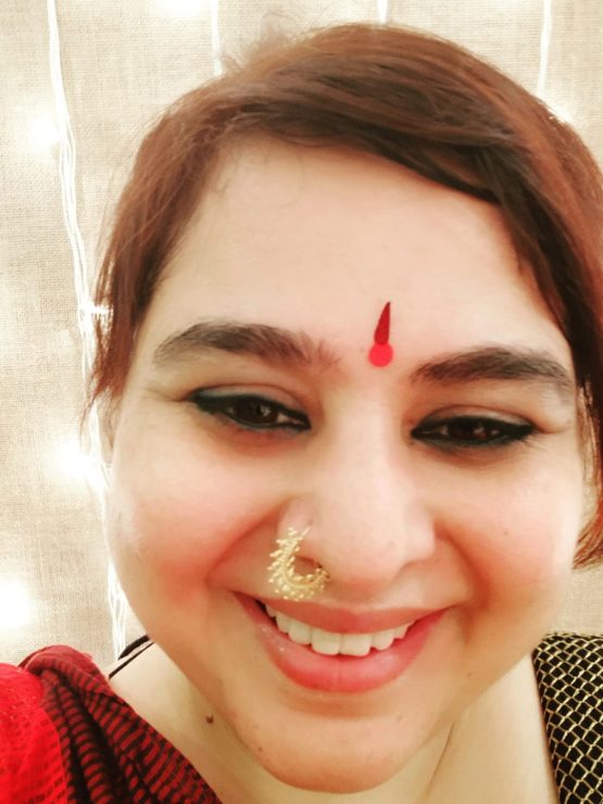 Headshot of Padmini, young indian woman smiling into camera with nose ring and red hair