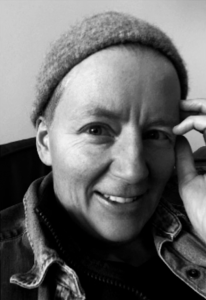 Black and white headshot of white woman wearing a beanie hat with one hand touching her face