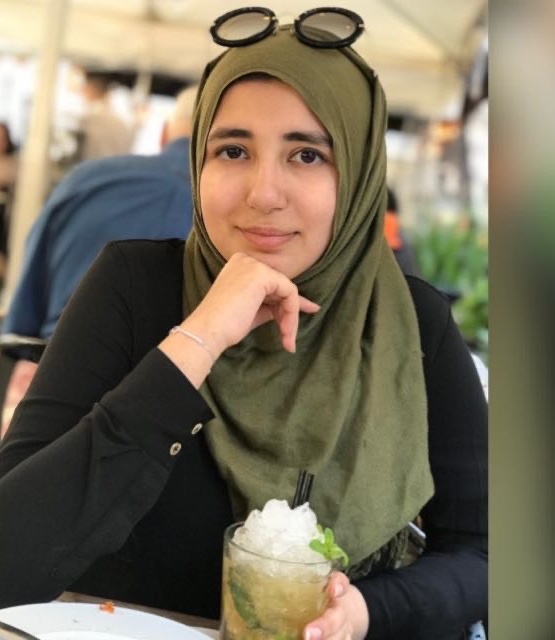 A woman wearing a green hijab is smiling as she drinks a cold drink with lots of ice