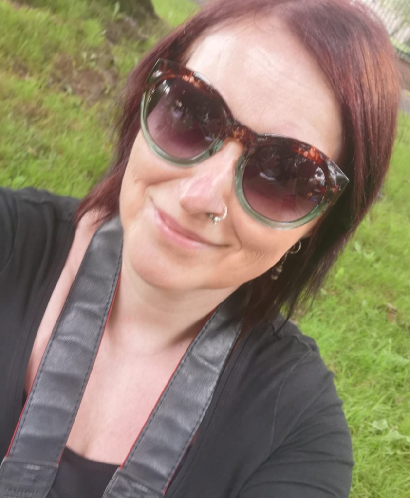 A white woman with a nose ring wearing dark sunglasses and smiling
