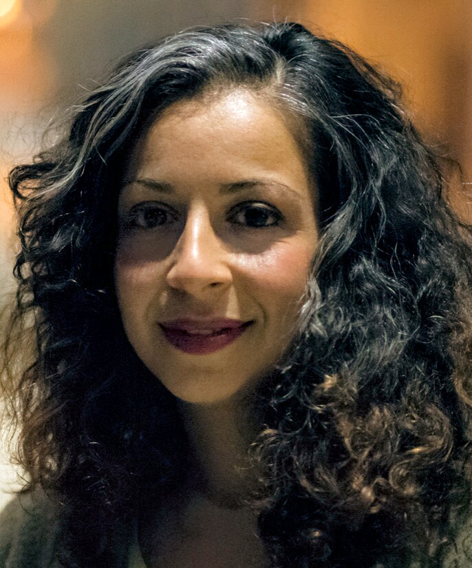 A portrait of a woman wearing dark purple lipstick. She has loose dark curly hair