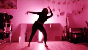 A woman wearing black leggings and a black top is dancing in a room that is lit by a red light