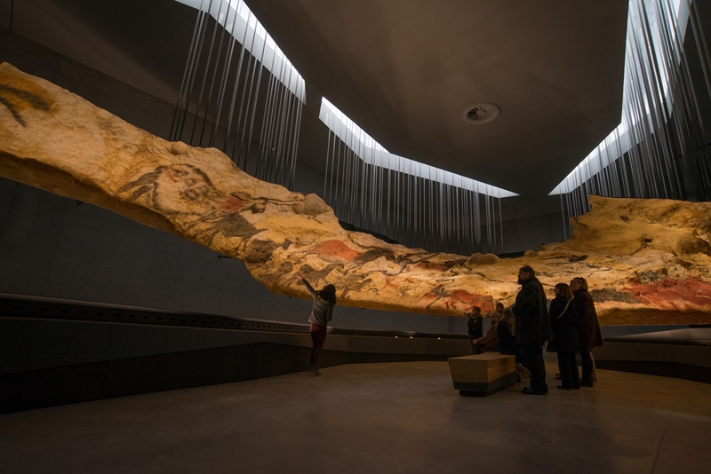 A recreation of the cave with projected lights onto a hanging model on display at Lascaux, with figures viewing in the gallery