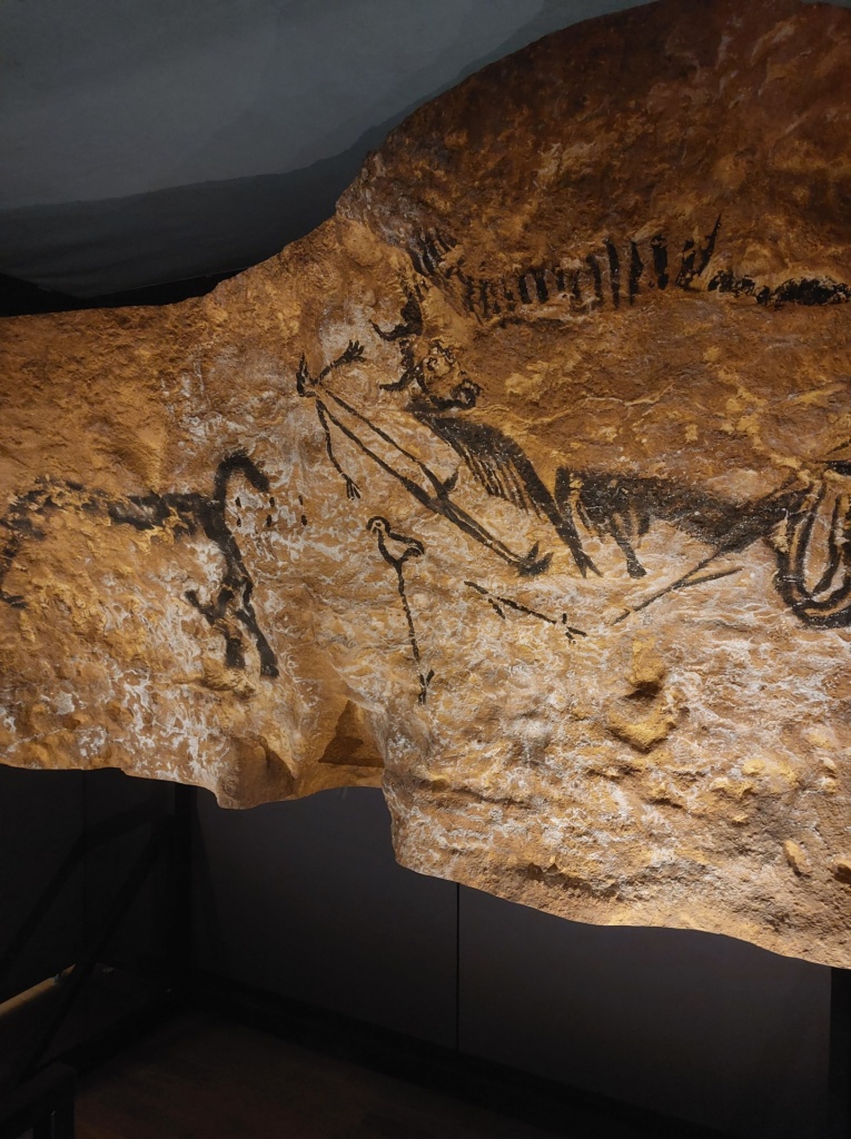 A replica of a piece of Lascaux cave wall, painted to represent from left to right a bull, a human figure, a bird with long legs, and another large animal
