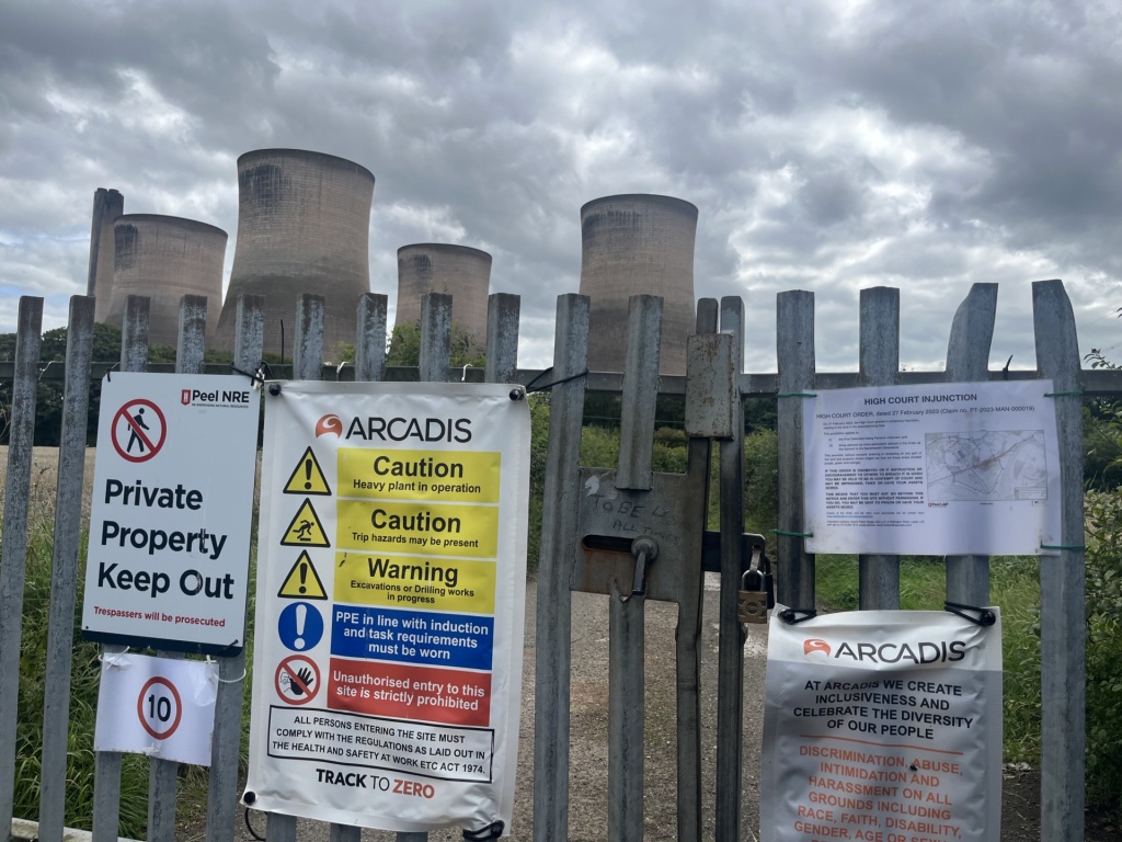 four concrete cooling towers behind a locked gate covered in notices about site security