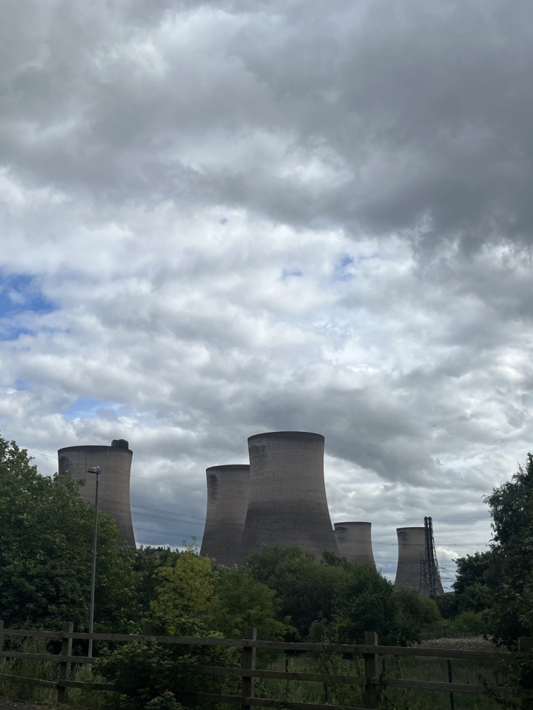 four cooling towers peeking out behind trees on a grey cloudy day