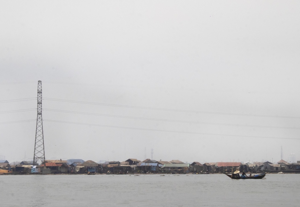 Makoko, seen from the water on an overcast day, a collection of low buildings with power lines overhead