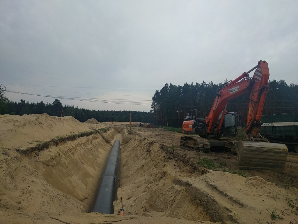 A pipeline being laid in dug ground in a dirt area with trees surrounding