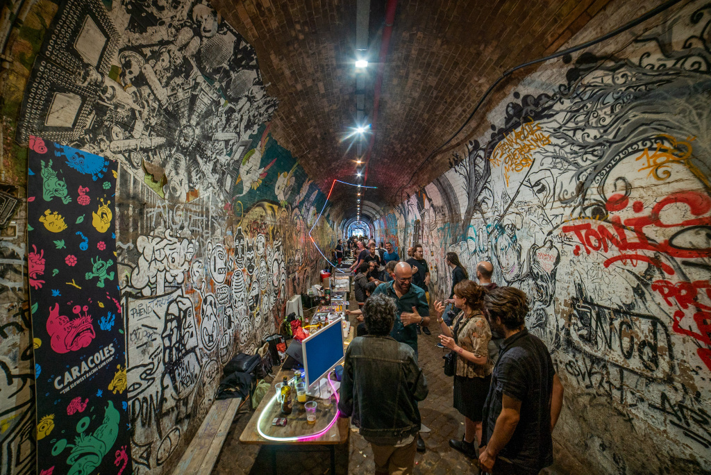 people in lit graffiti covered tunnel with interactive computers and playable games