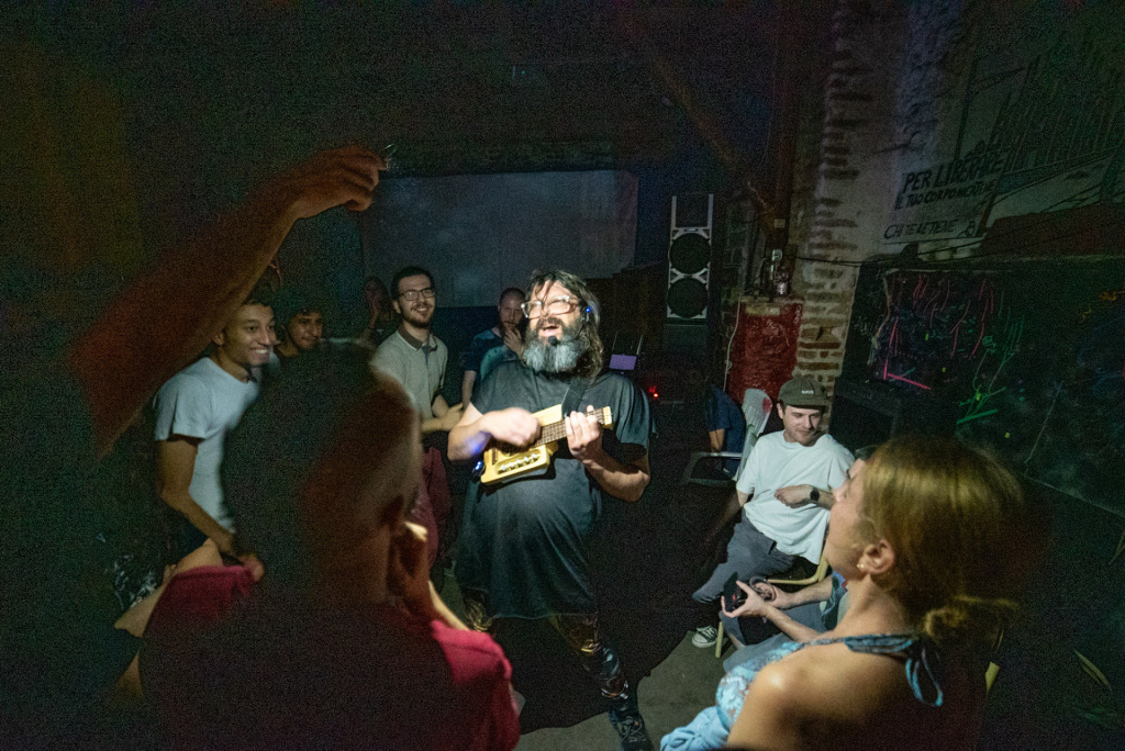 person giving an impassioned musical performance in a dark room lit by a spotlight and surrounded by enthusiastic people watching on