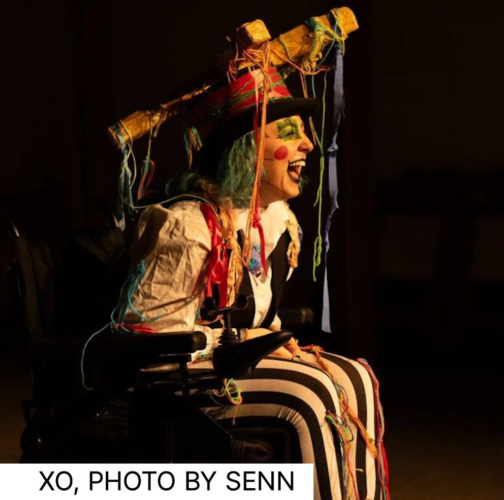 XO in a clownish outfit and makeup performing in wheelchair