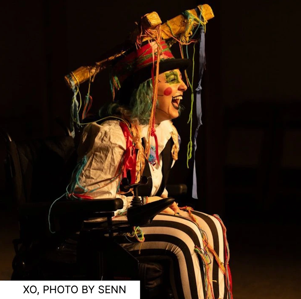 XO in a clownish outfit and makeup performing in wheelchair