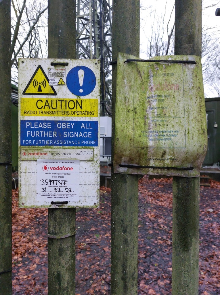 Signs attached to a fence, with warnings and cautions about the site as a radio tower