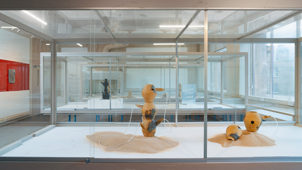 A sideview of a gallery display case featuring pots embedded in sand with tubes emerging from them