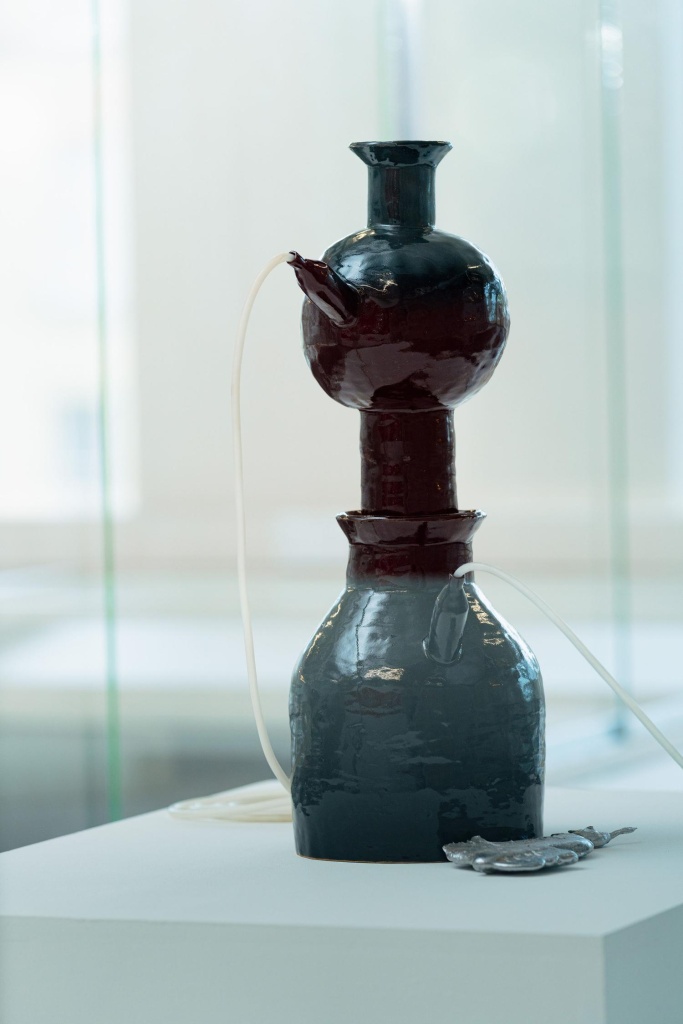 A ceramic pot with a shiny finish that has a spout at the top, a tube is coming out of the spout