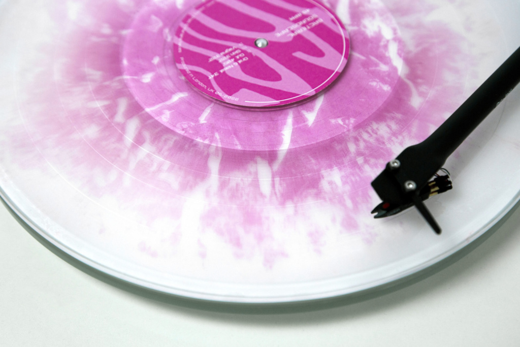 A close up of a clear vinyl record with pink dye patterning