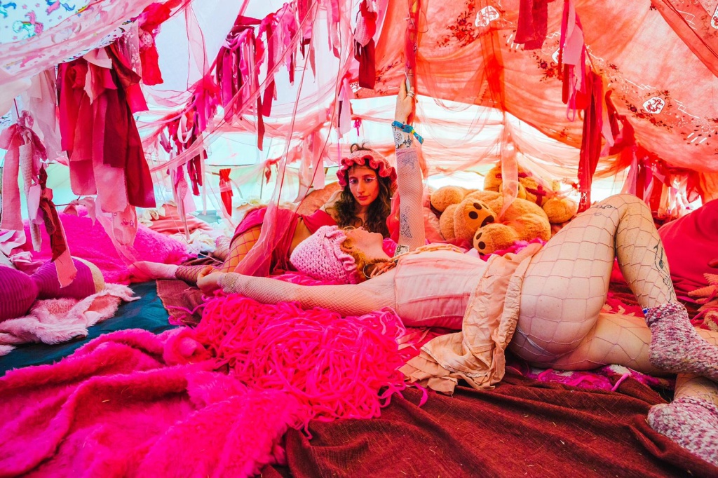 cute cartel performers lounging inside a tent of fabrics at a festival