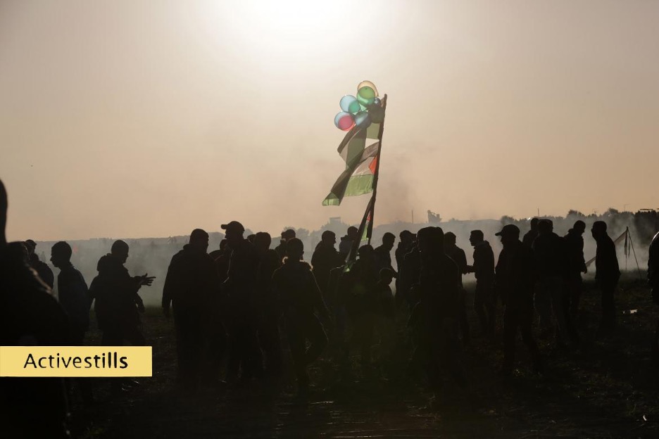 people in silhouette walking with Palestinian flags and balloons attached