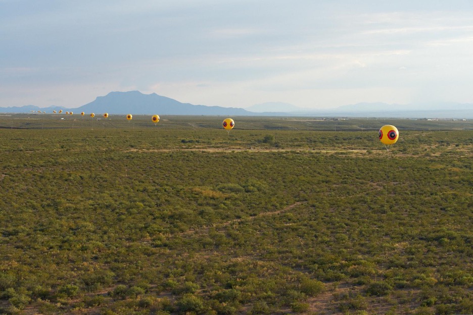 large balloons on a vast plain, sat in a line with distance between them, a hill in the background