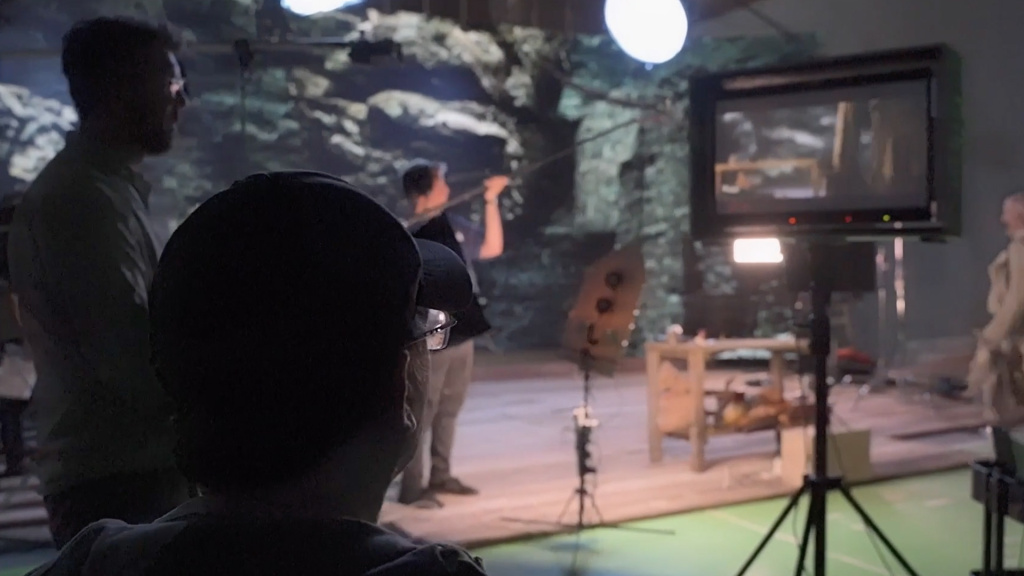 shot of a person's head as they look over a movie set, at the monitor and crew setting up a shot