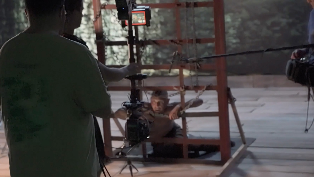 a virtual production set, a person is on the ground by some cage bars, a camera is tracking them