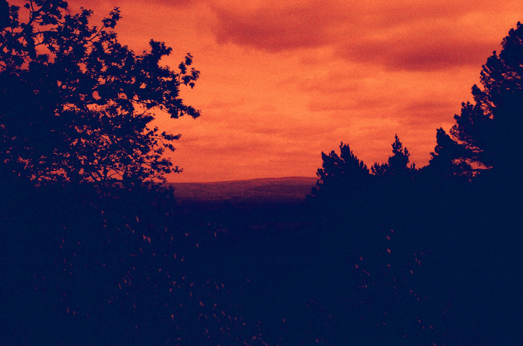 a redscale landscape of a large area silhouetted area seen from a high point with silhouetted trees framing
