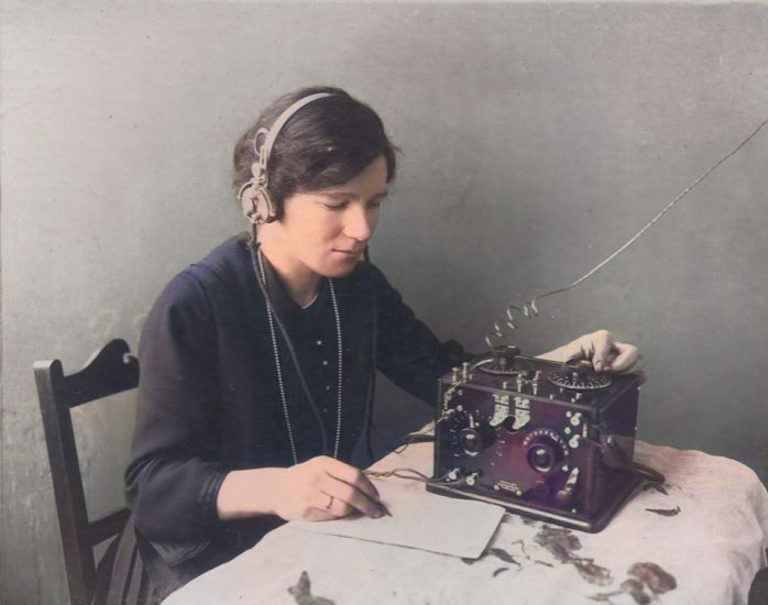 an early photograph of a woman sat at a table with headphones and a wireless radio