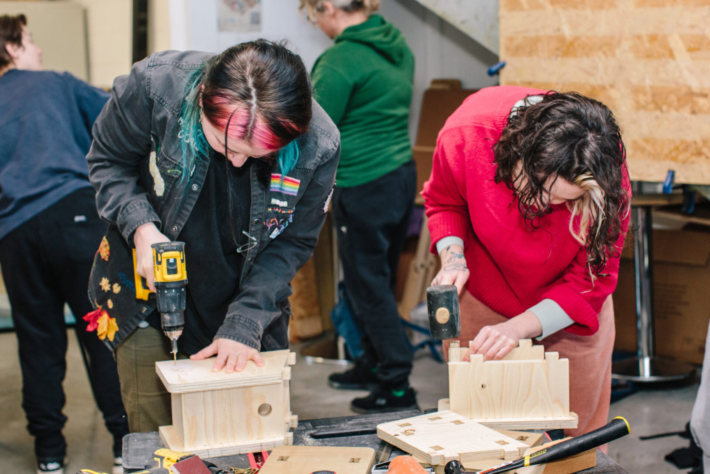 two people at a bench in a community workshop drilling into and assembling wood