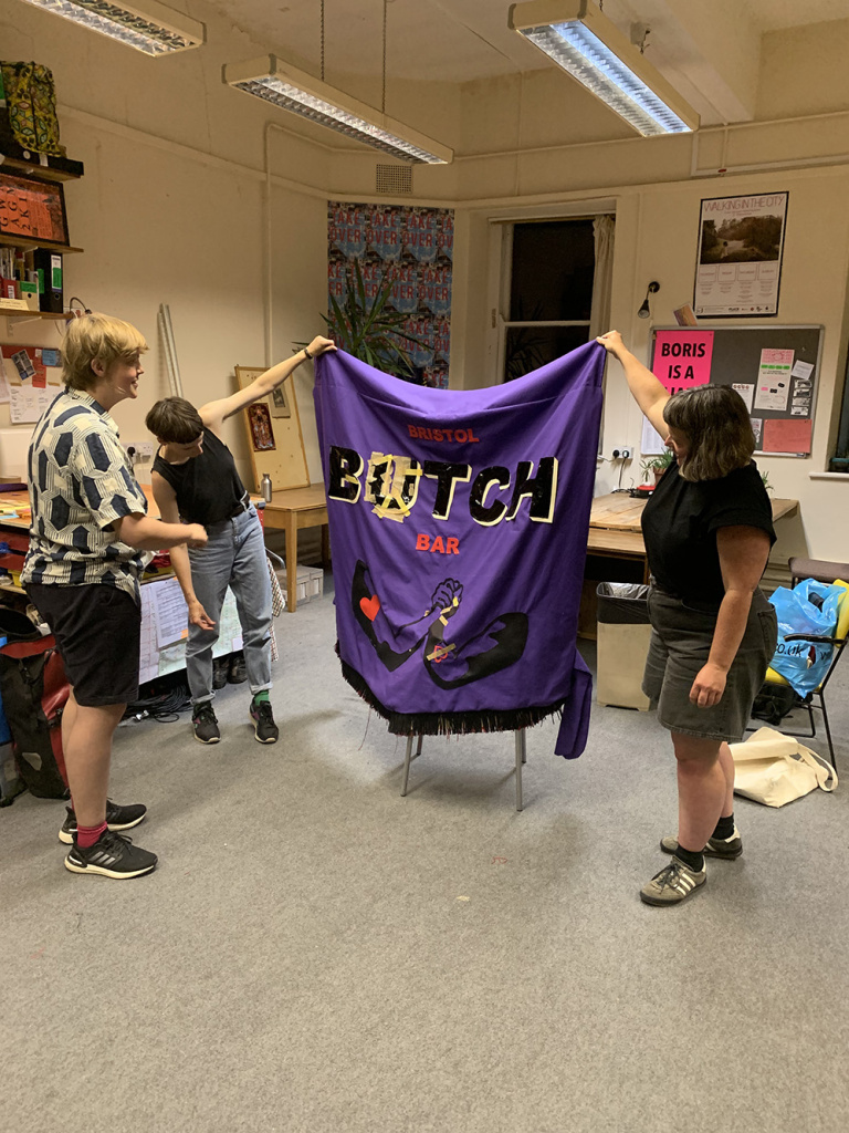 group of three people with large fabric banner reading bristol butch bar